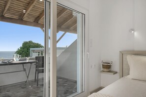 Quarto com uma grande porta de vidro deslizante que dá para uma varanda, uma cama com cabeceira, mesa de cabeceira e uma pequena prateleira com um cesto.