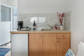 A compact kitchen with a built-in refrigerator, a coffee maker, and a wine bottle on the counter.