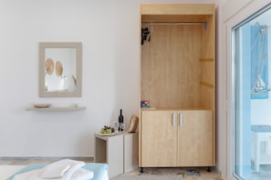 A room with a bed, a wooden wardrobe, a small table with a bottle and a bowl, and a mirror on the wall.