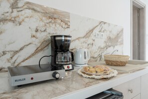 A kitchen with a coffee maker, a kettle, a bread basket, and a microwave.