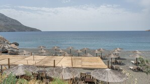 Une zone aménagée sur la plage, avec des parasols et des chaises, offrant une vue dégagée sur la mer, et une colline rocheuse en arrière-plan.
