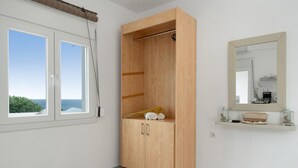 Une chambre dotée d’une armoire, d’une fenêtre donnant sur un paysage agréable, d’un miroir et d’une étagère ornée d’objets décoratifs.