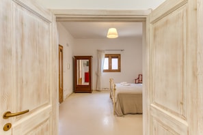A hallway leading to a bedroom with a bed, a mirror, and a window.