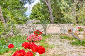 A stone wall, red flowers, and a bench in a garden setting.