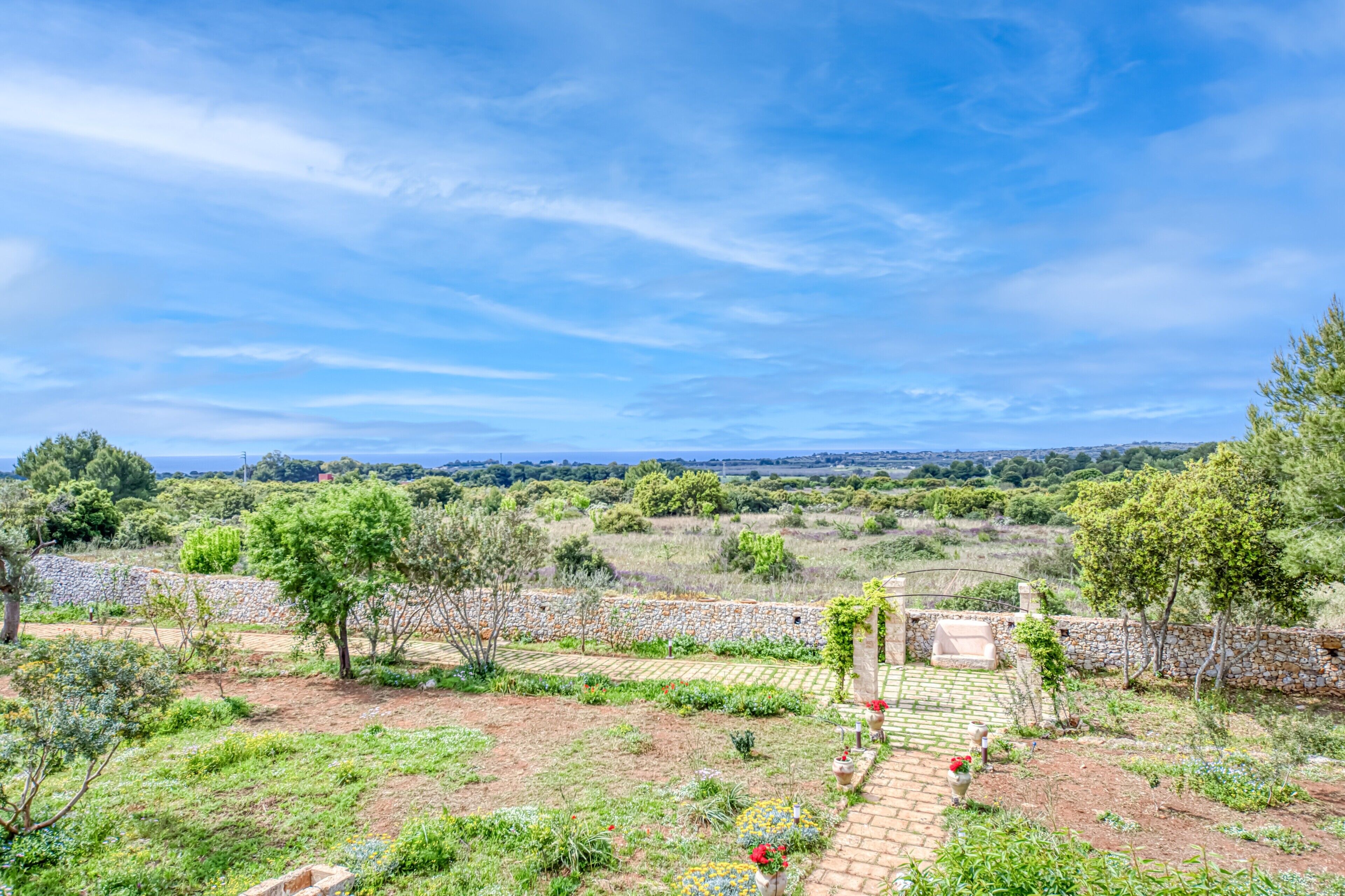 A garden with a stone wall, a paved patio, and a view of the countryside.