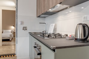 Une cuisine moderne équipée d’une cuisinière à gaz, d’une bouilloire en acier inoxydable et d’un petit plan de travail.
