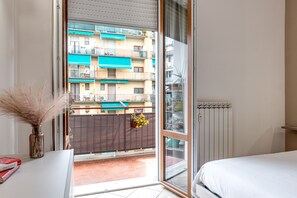 A bedroom with a sliding glass door leading to a balcony, a radiator, and a small table with a vase and books.