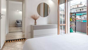 A bedroom with a bed, a dresser, a mirror, and a view of the outside.