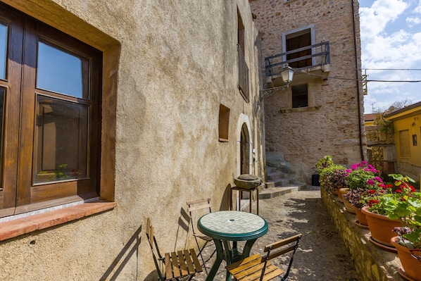 A stone building with a window, a small table with chairs, and potted plants.