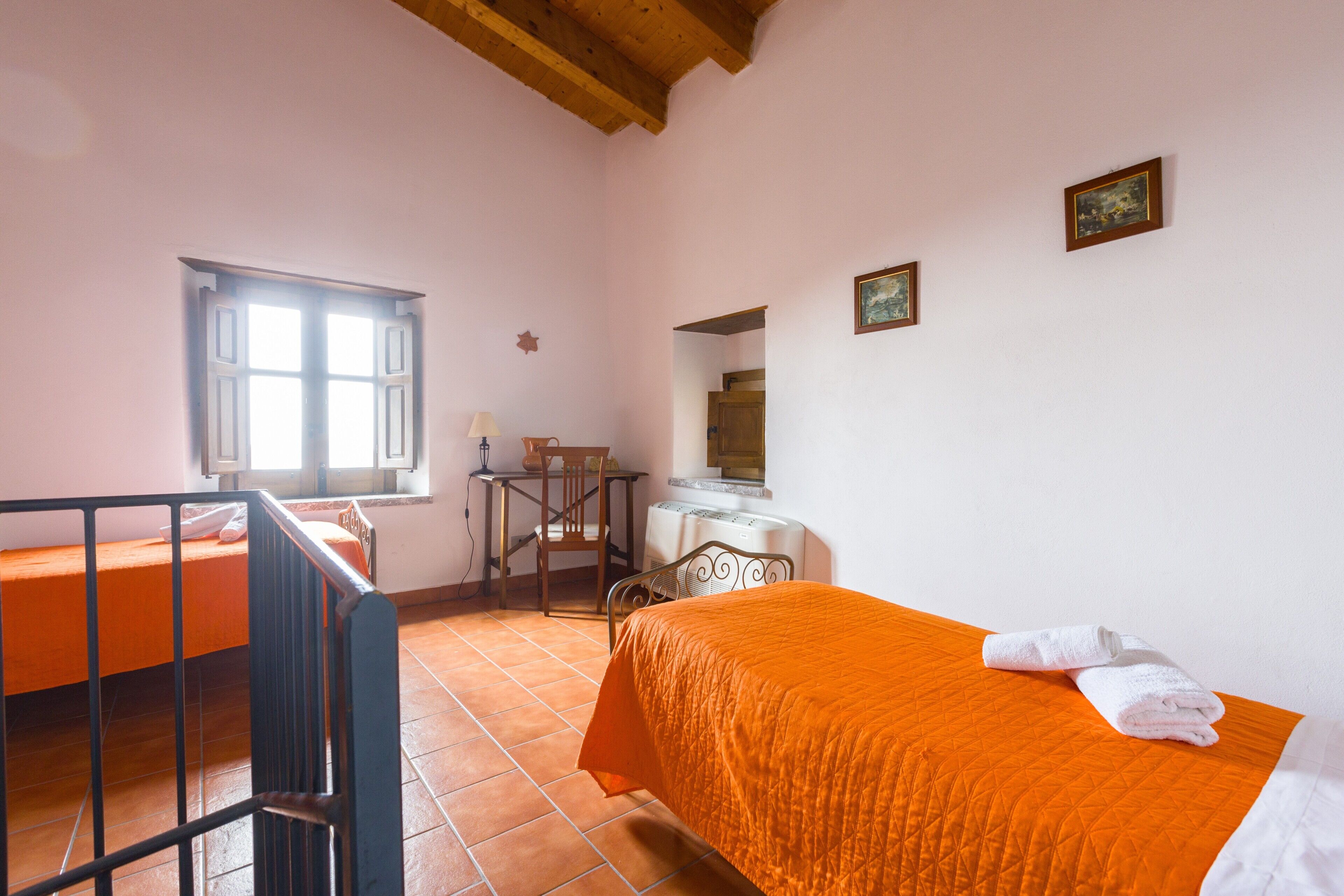A bedroom with a bed, a desk, a chair, a window, and a radiator.