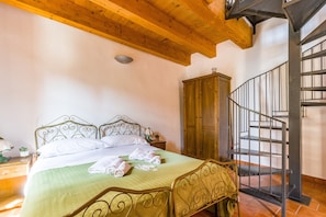 A bedroom with a bed, wooden headboard, a nightstand, a wooden wardrobe, and a spiral staircase.