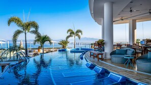 A pool area with a view of the sea, palm trees, and a dining area with tables and chairs. - HOLT Grand Miramar Residences (Puerto Vallarta)