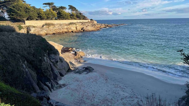 Un paysage côtier avec une plage de sable, des falaises rocheuses et un mur de pierres.