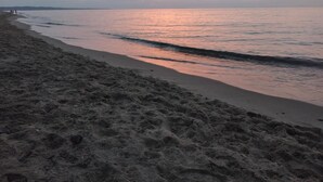 Una playa con atardecer, agua tranquila y orilla arenosa.