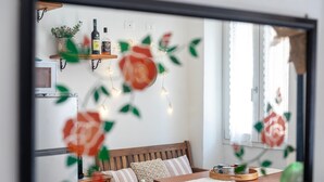 Una habitación con una mesa de madera, un sofá, un televisor y un estante en la pared con botellas y una planta.