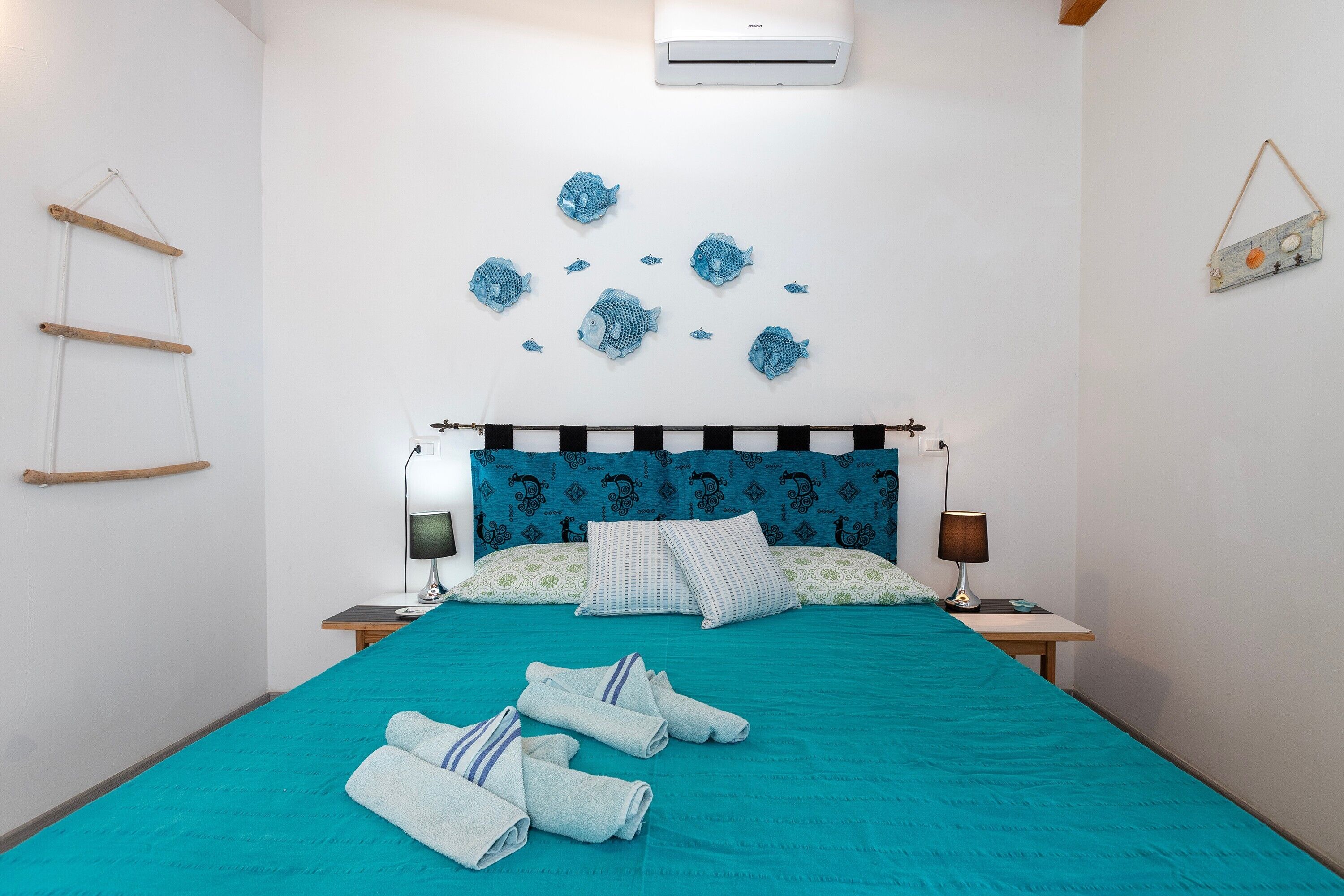 A bedroom with a bed, pillows, a bedside table, a lamp, and wall decorations.