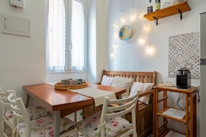 A cozy kitchen with a wooden table, white chairs, a coffee machine, and a shelf with kitchen items. - Holiday Home 'De Mirto' with Wi-Fi and Air Conditioning (Sennori)