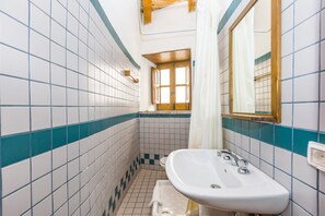 Une salle de bain avec des carreaux blancs et turquoise, un lavabo blanc et une fenêtre avec un cadre en bois.