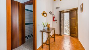 Un pasillo con puertas de madera, un muro con azulejos, una pequeña mesa con un florero y un extintor.