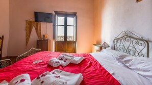 Una habitación de hotel con cama, ventana, televisor y escritorio con lámpara.