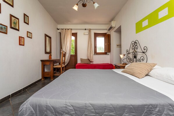 A bedroom with a bed, a desk, a chair, a window with curtains, and a wall-mounted air conditioner.