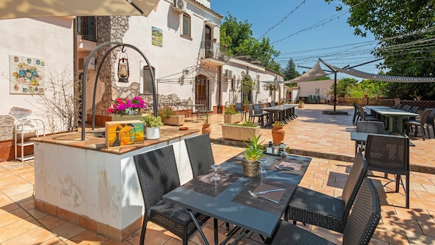 Eine Terrasse im Freien mit Tischen und Stühlen, eine Steinsäule und ein Gebäude mit Balkon.