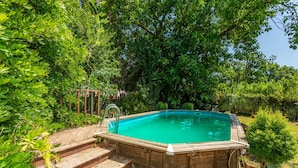 Eine Holzterrasse führt zu einem Swimmingpool, der von üppiger Vegetation umgeben ist.