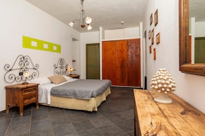 Un dormitorio con una cama, mesitas de noche, un aparador de madera, un espejo y una puerta.