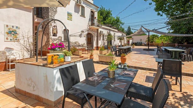 Une terrasse extérieure avec des tables et des chaises, un mur en pierre et un bâtiment doté d’un balcon.