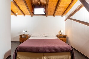 A bedroom with a wooden ceiling, a skylight, a bed with a red blanket, two bedside tables with lamps, and a white wall. - Room 'Cosimo' with Mountain View, Wi-Fi and Air Conditioning (Taormina)
