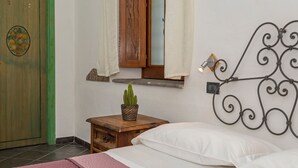 A bedroom with a bed, a wooden nightstand with a cactus, a mirror, and a wall-mounted light fixture. - Room 'Ninetta' with Mountain View, Wi-Fi and Air Conditioning (Taormina)