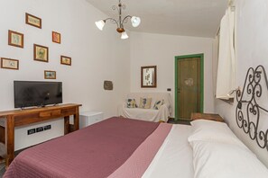 A bedroom with a bed, a TV, a wooden desk, a green door, and several framed pictures on the wall.