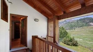 Una escalera de madera lleva a un balcón con vistas a un valle verde y montañas.
