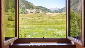 Vista desde una ventana a un valle verde con montañas, cielo despejado y marco de madera.