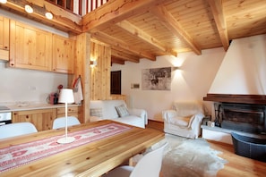 A wooden interior with a dining table, white sofas, a fireplace, and wooden cabinets.