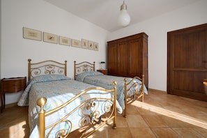 A bedroom with two beds, a wooden wardrobe, a nightstand, and framed pictures on the wall. - Holiday Home 'Il Quercione' with Private Terrace, Wi-Fi and Air Conditioning (Suvereto)