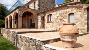Un bâtiment en pierre doté d’un balcon, de portes en arc de cercle et d’un grand pot en terre cuite.