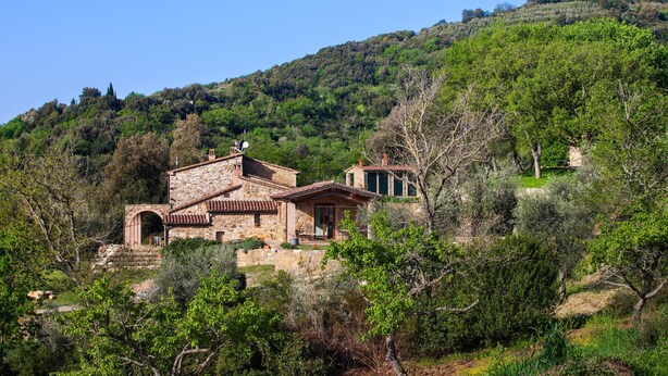 Une maison en pierre avec un toit de tuiles, entourée de verdure et de collines.