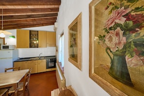 A kitchen with wooden cabinets, a dining table, and a painting of flowers. - Holiday Home 'La Carraia' with Private Terrace, Wi-Fi and Air Conditioning (Suvereto)