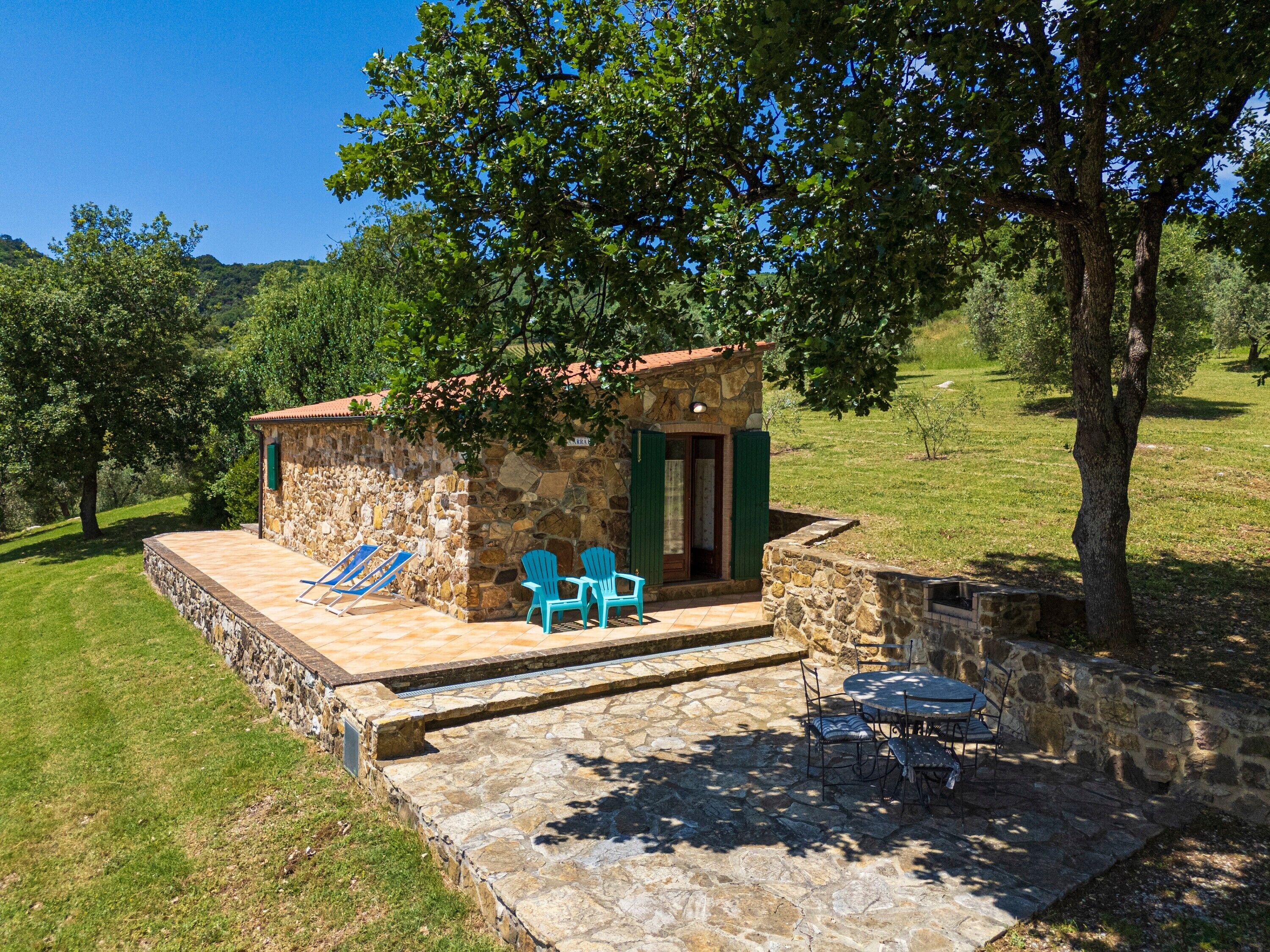 Ein Steinhaus mit einer Terrasse, zwei blauen Stühlen und einem Tisch.