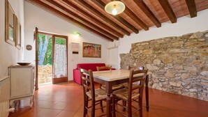 A dining area with a wooden table and chairs, a red sofa, a stone wall, and a ceiling with wooden beams. - Holiday Home 'La Carraia' with Private Terrace, Wi-Fi and Air Conditioning (Suvereto)