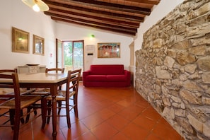 A dining area with a wooden table and chairs, a red sofa, and a stone wall. - Holiday Home 'La Carraia' with Private Terrace, Wi-Fi and Air Conditioning (Suvereto)