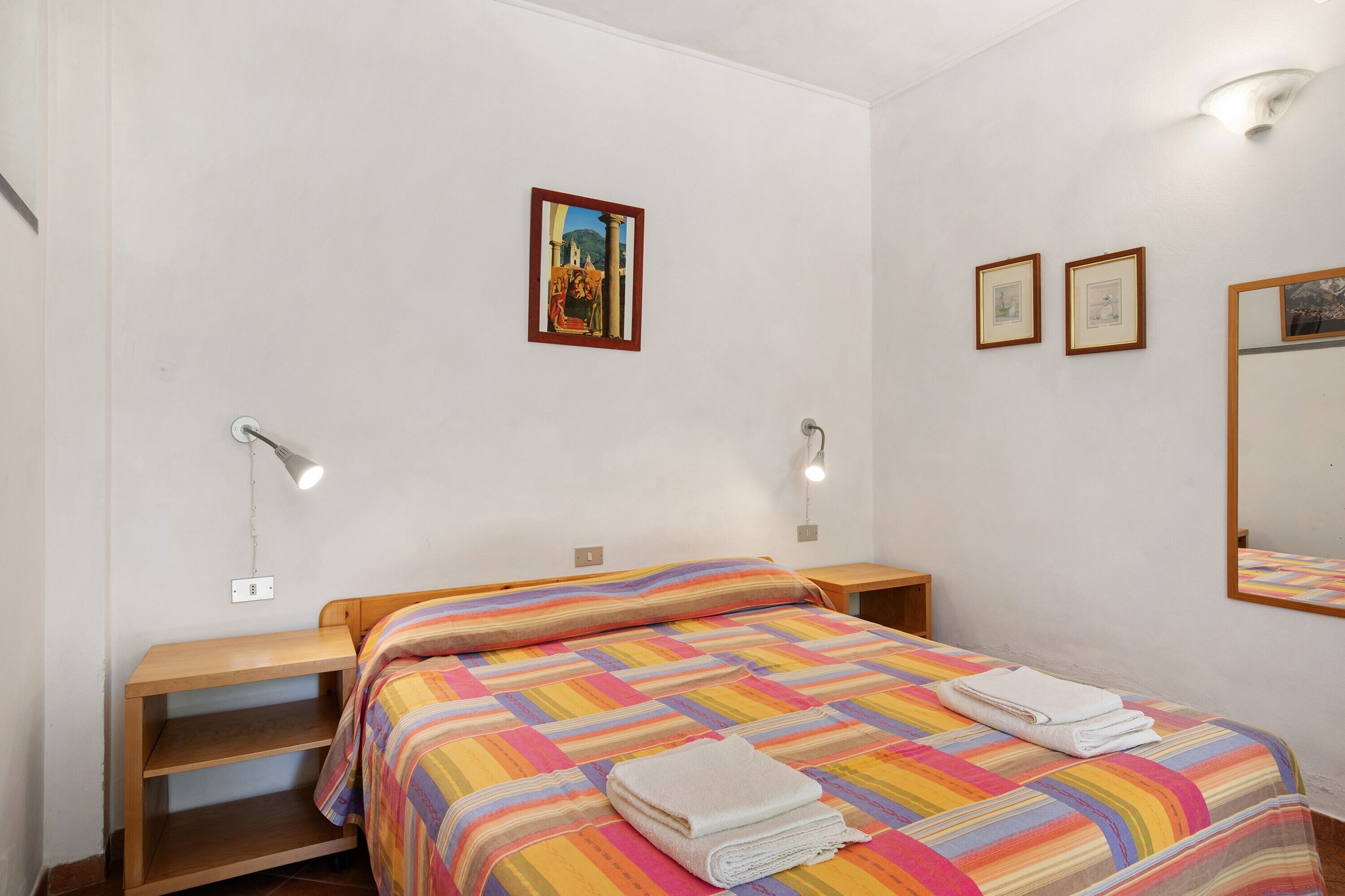 Une chambre à coucher avec un lit, des tables de chevet, un miroir et des lampes fixées au mur.