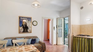 A compact living space with a sofa, dining table, kitchen area, and a poster on the wall. - Holiday Home 'Chiara' with Private Terrace, Wi-Fi and Air Conditioning (Marina di Pietrasanta)