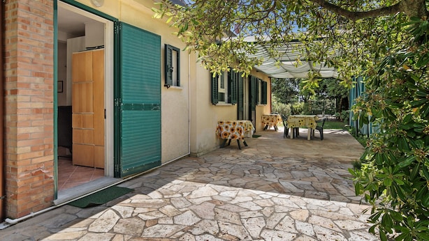 A stone-paved patio with a table and chairs, a wooden cabinet, and a green shuttered door. - Holiday Home 'Chiara' with Private Terrace, Wi-Fi and Air Conditioning (Marina di Pietrasanta)
