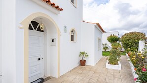 A white building with a white door, a small potted plant, and a tiled walkway.