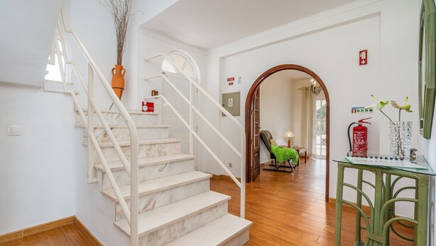 A staircase with white railings, a green chair, and a glass table with a vase.