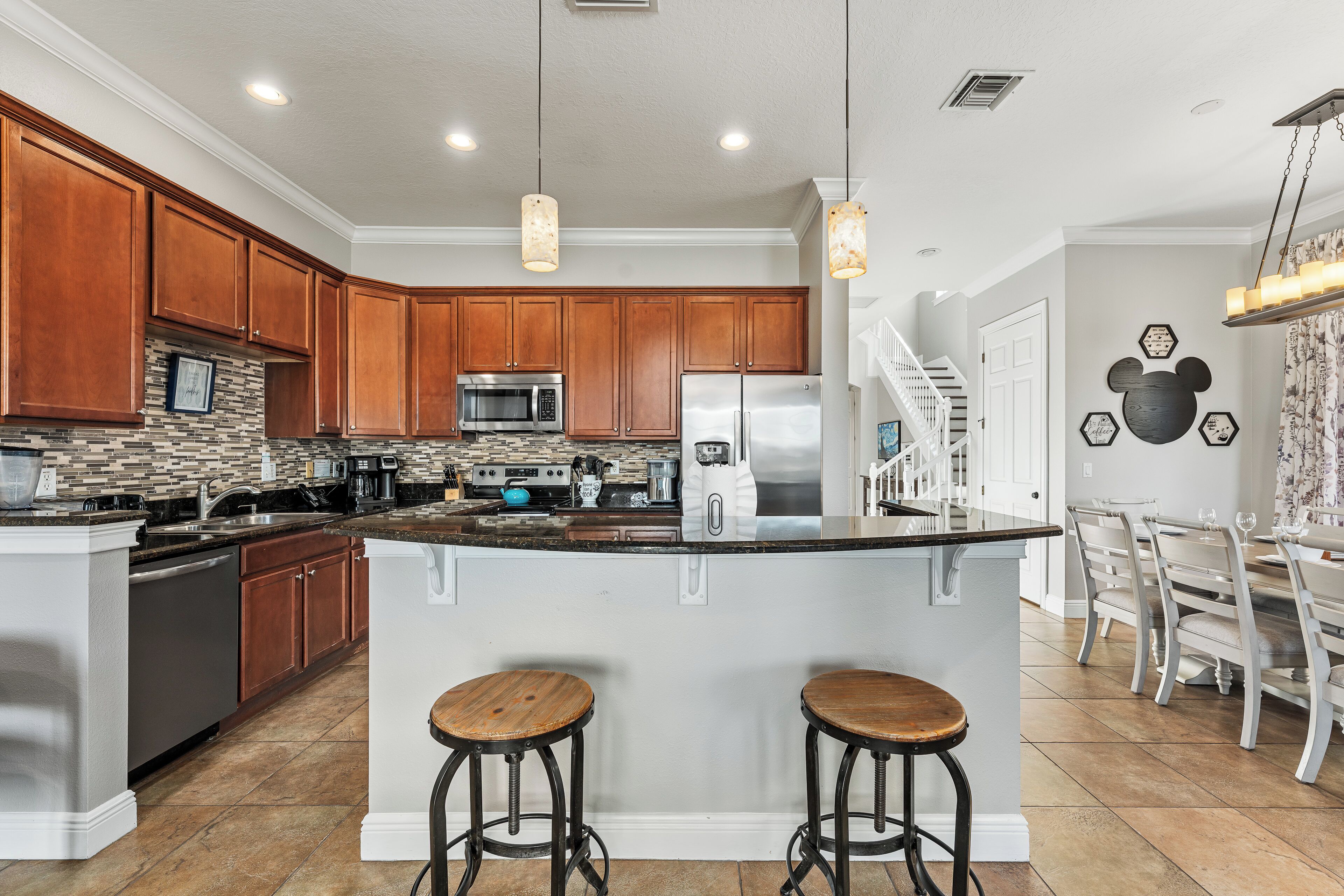 A modern kitchen with wooden cabinets, a central island with stools, stainless steel appliances, and pendant lighting.