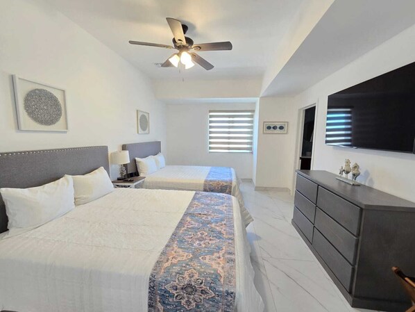 A hotel room with two beds, a ceiling fan, a TV, and a dresser.