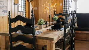 Une table de salle à manger en bois, avec des chaises noires, un centre de table composé de bougies et un panneau sur le mur présentant des informations sur les élans.